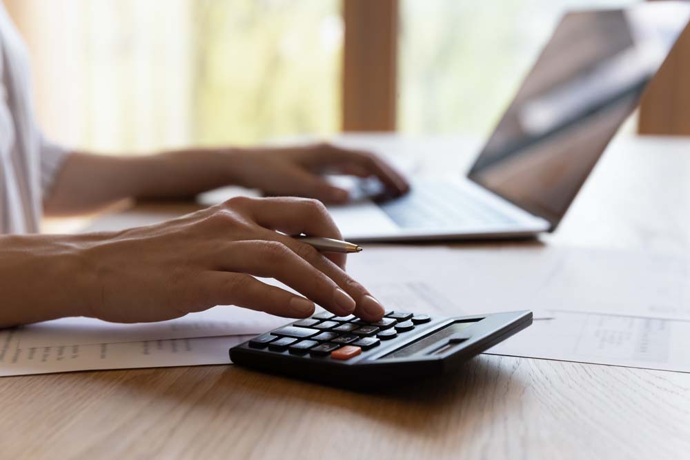 Womans hands working at desk with laptop and calculator.